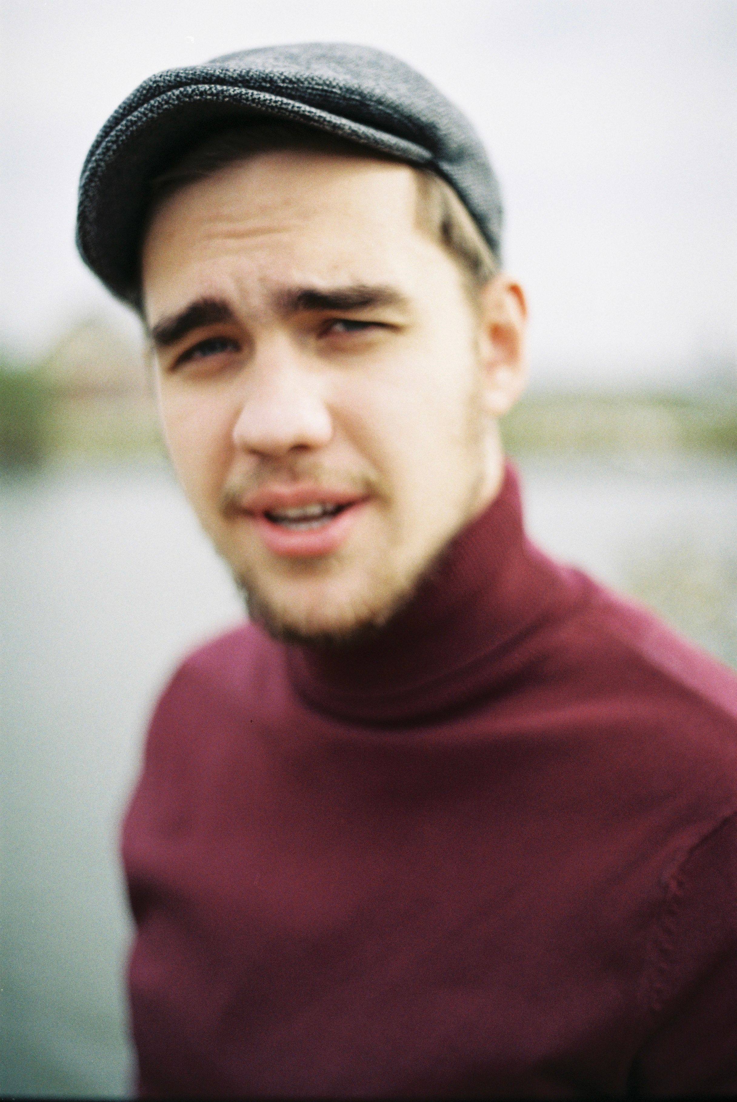 Portrait of a fashionable young man wearing a burgundy turtleneck and flat cap outdoors.