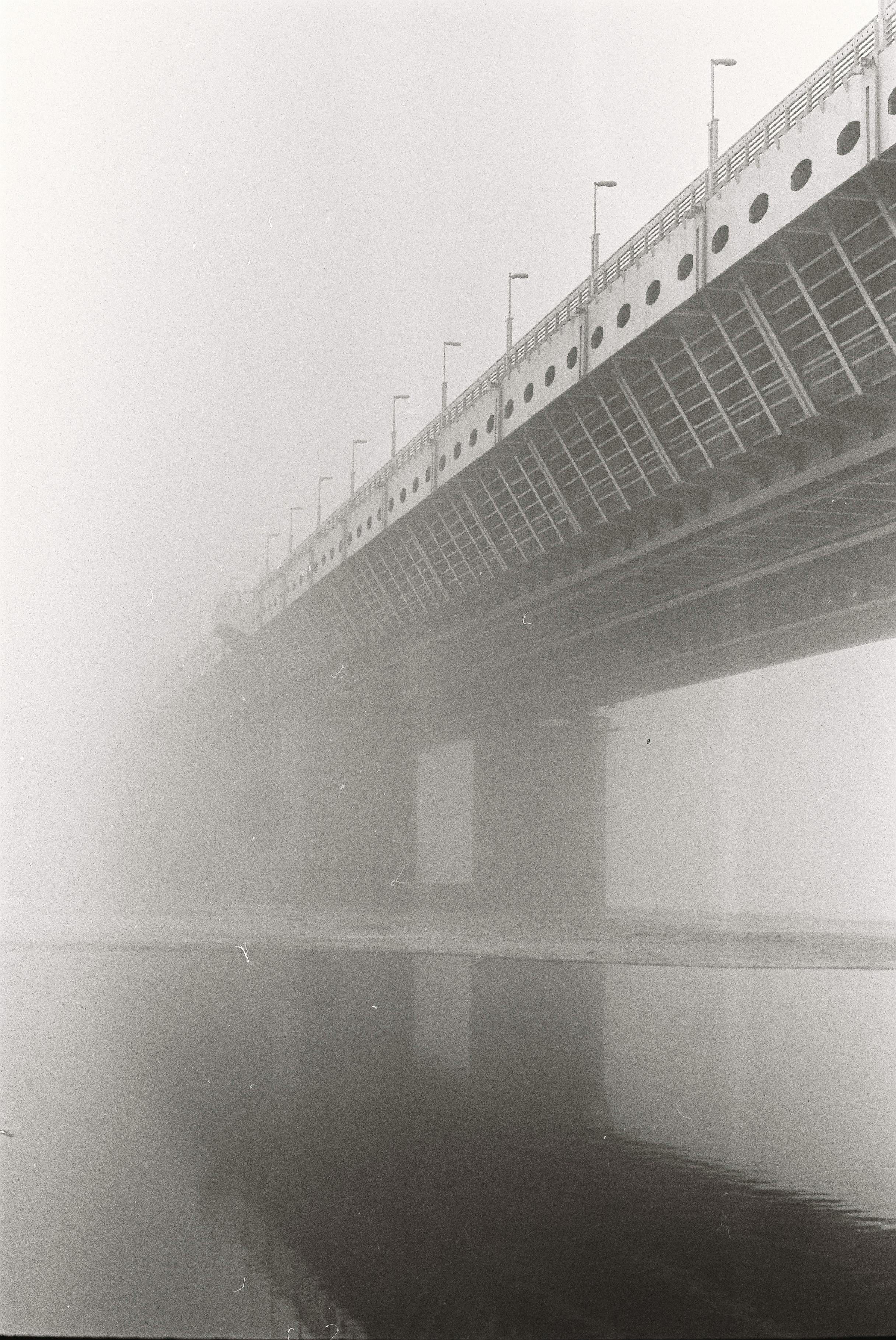 Atmospheric grayscale image of a bridge shrouded in fog over water.