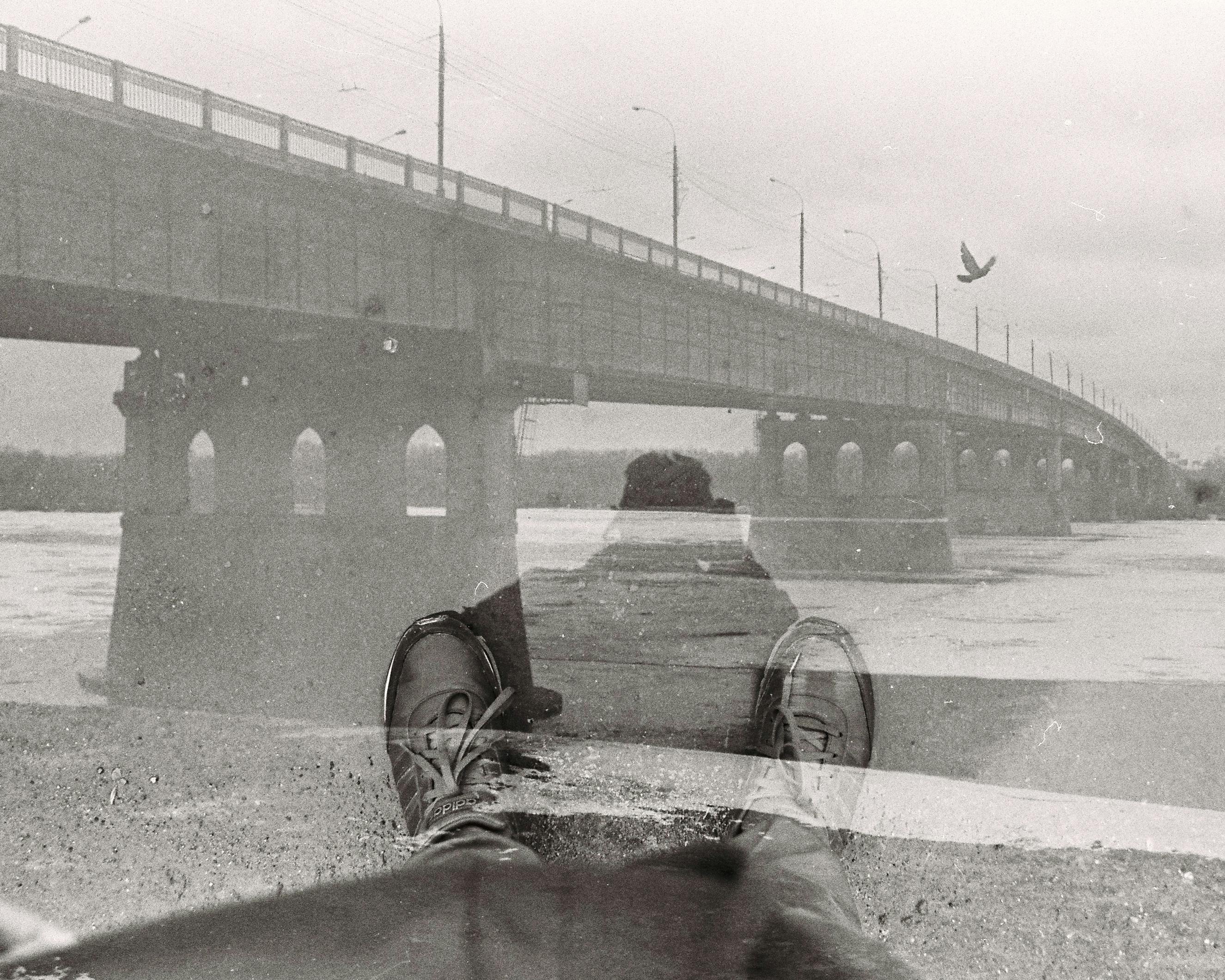 Artistic black and white double exposure featuring a bridge and human feet in an outdoor setting.