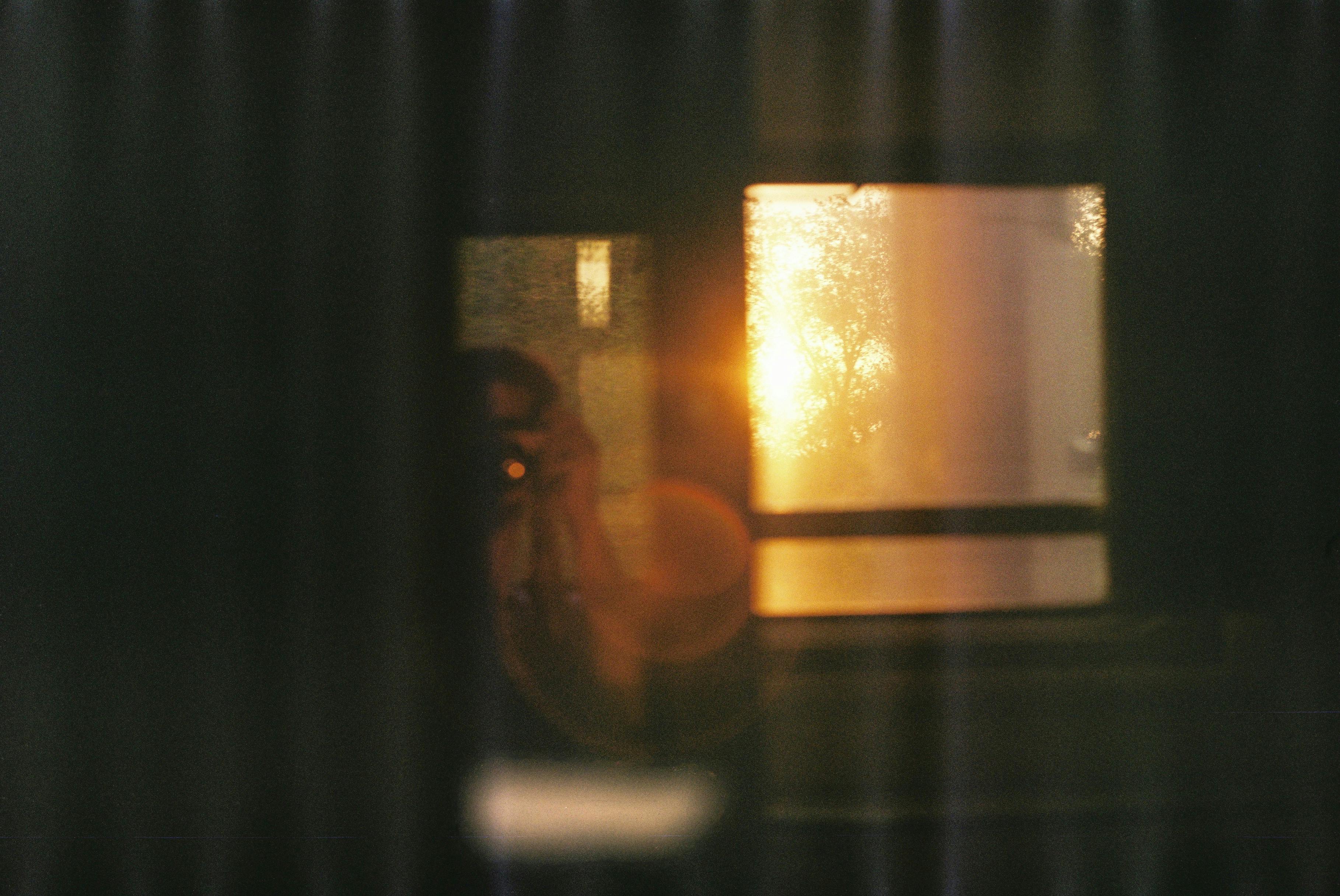 A blurred reflection of a person with sunset through a window creating a warm glow.