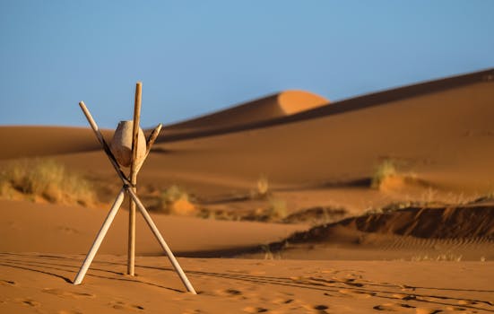Peaceful desert landscape at Merzouga with sand dunes and wooden tripod under clear blue sky.