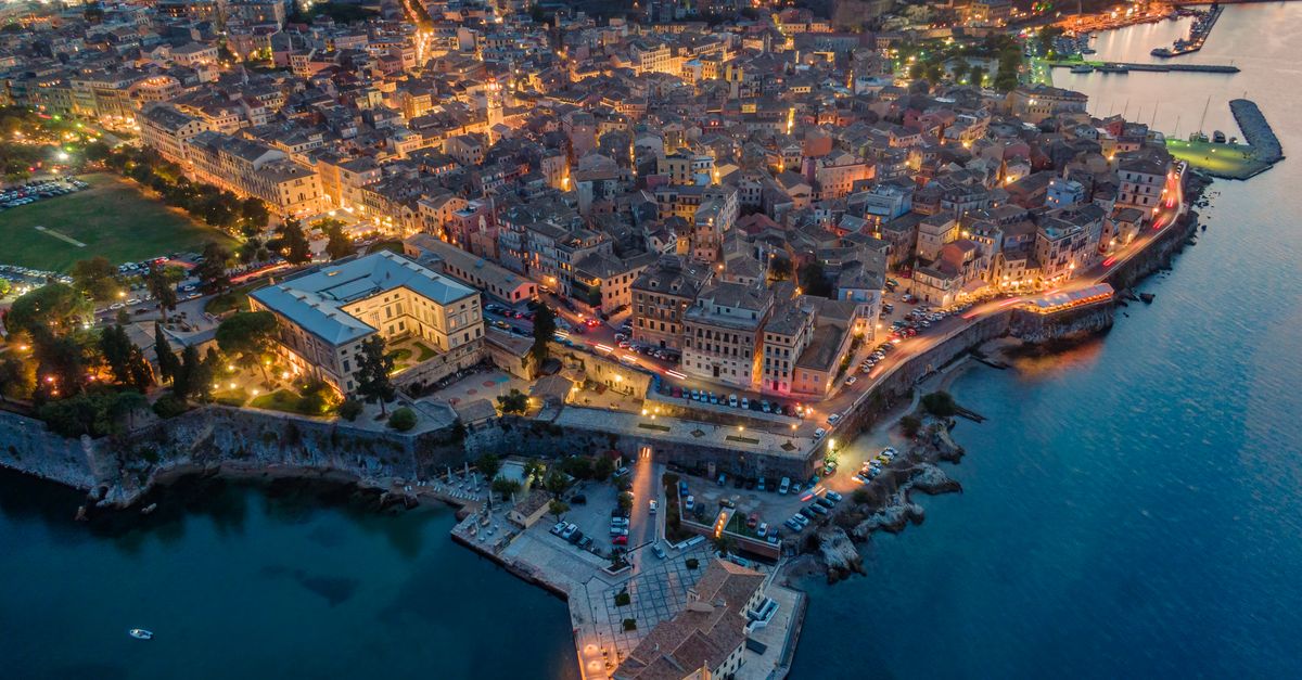 Stunning aerial view of Corfu city illuminated at night, reflecting on the sea.