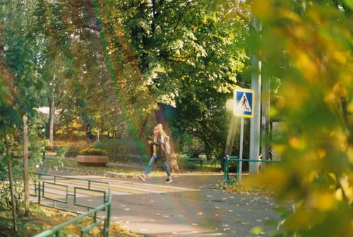 Free A woman strolls along a serene park path on a sunny day. Vibrant green foliage surrounds her. Stock Photo