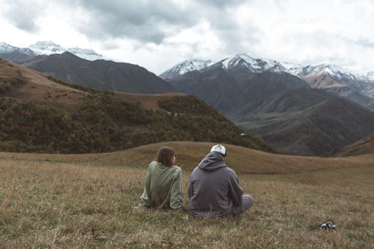 A couple sitting on grassland, admiring scenic mountains in autumn. Perfect for travel and nature themes.