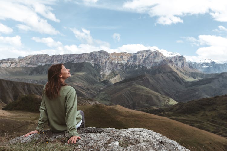 A Woman Sitting On The Rock While Breathing Fresh Air From The Mountain