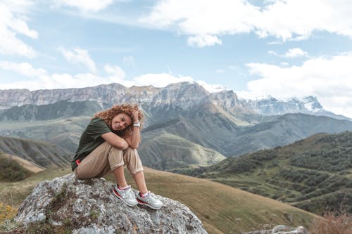 A Female Sitting on A Rock, Smiling in Mountains 