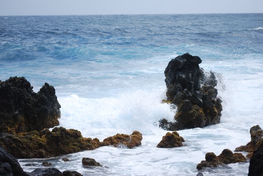 Captivating scene of ocean waves crashing against rocky shoreline with mossy boulders.