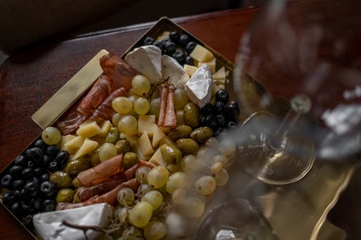 A stylish cheese and charcuterie board with olives, grapes, and a wine glass on a tray indoors.