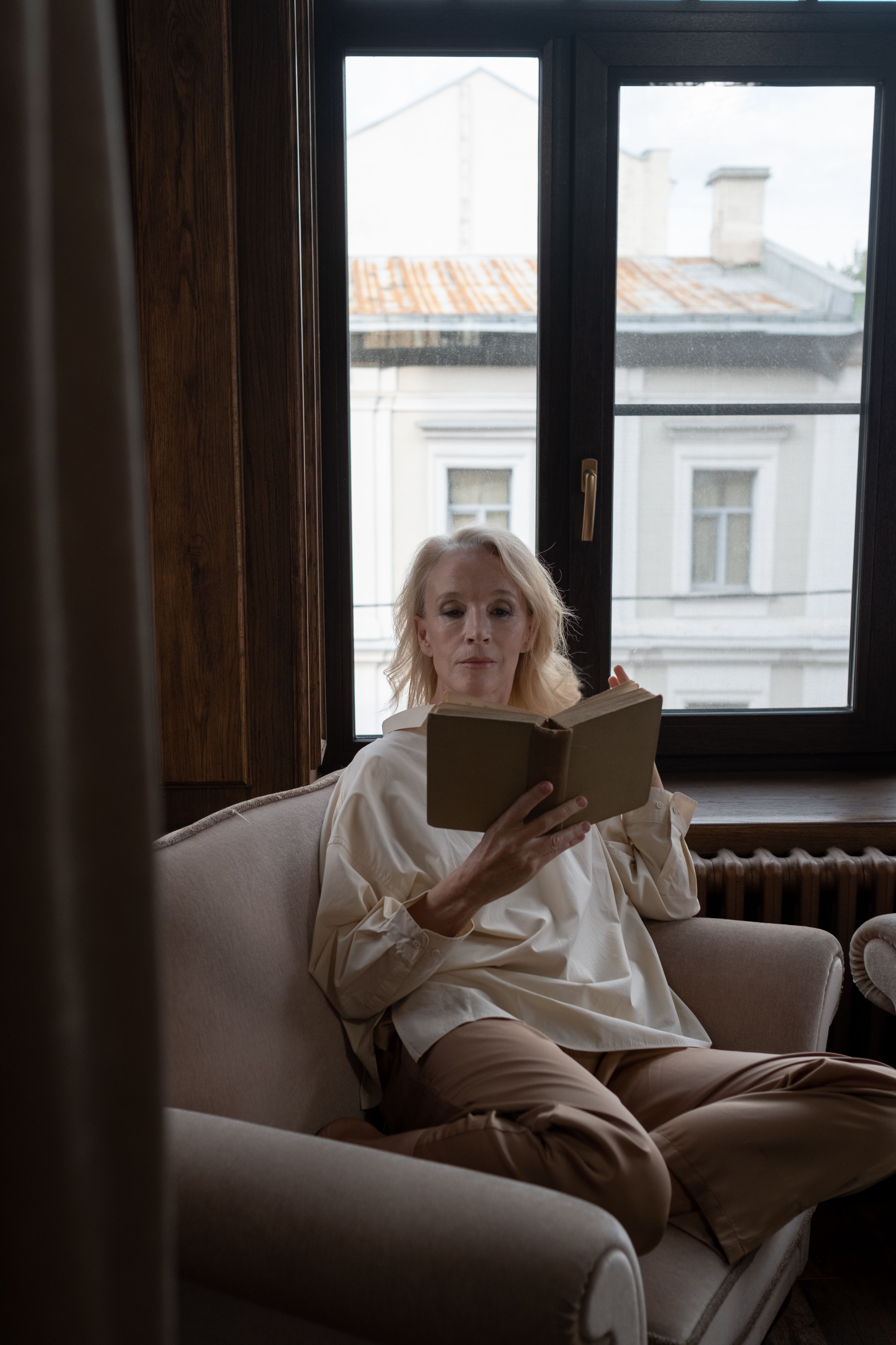 A senior woman enjoys reading in a cozy armchair by a window.. senior, woman, enjoys