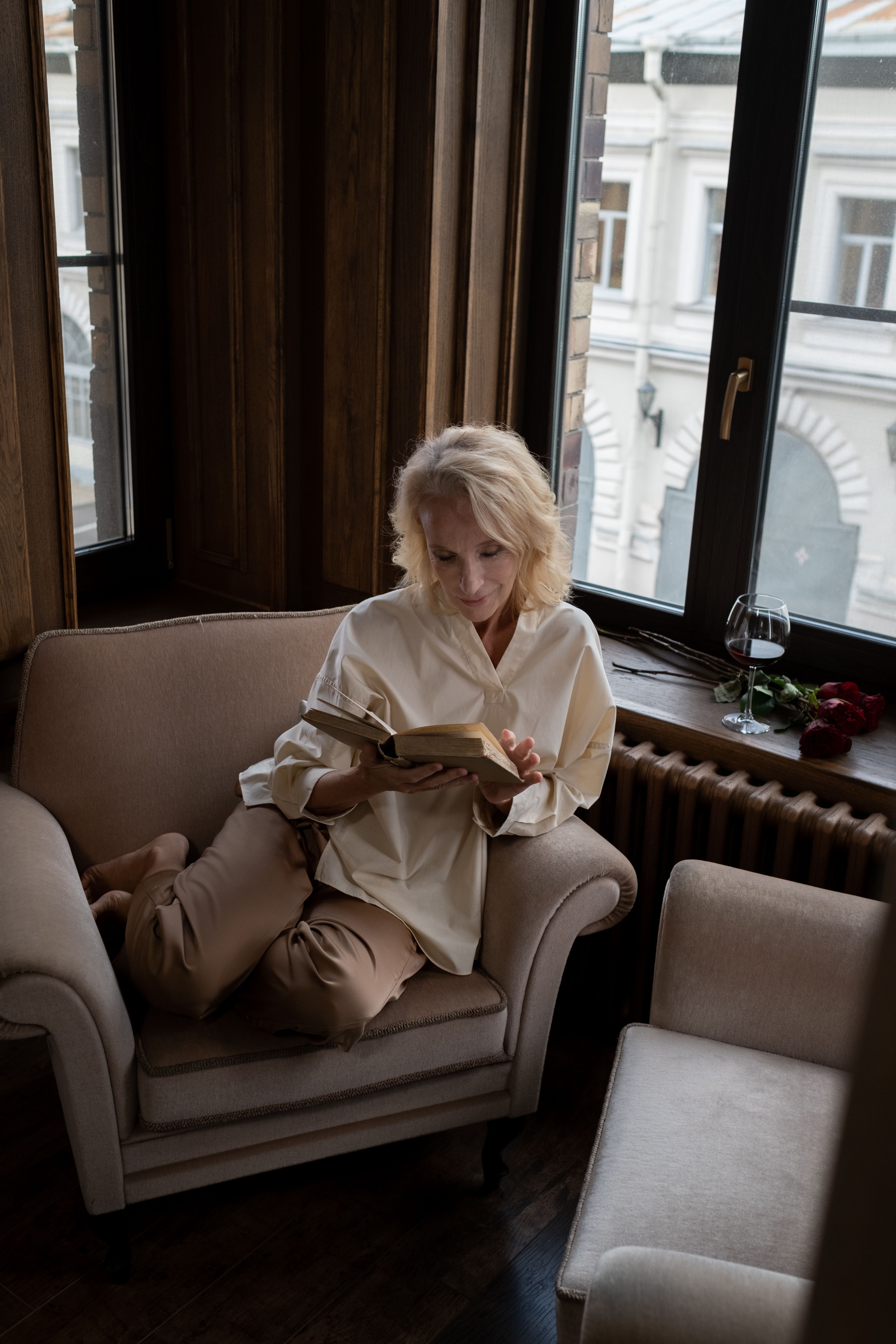 Senior woman reading a book in an armchair by the window indoors.. senior, woman, reading
