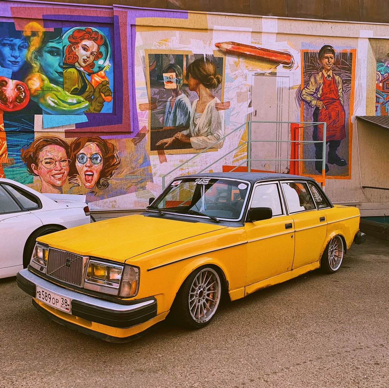 Classic yellow car parked in front of an artistic mural on a street in Irkutsk, Russia. Vibrant urban scene.