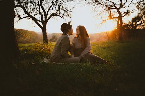 Couple Sitting on Green Grass Field during Sunset