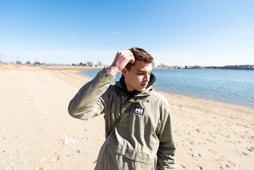 A stylish young man in a jacket enjoys a sunny day at a beach in Boston, MA.