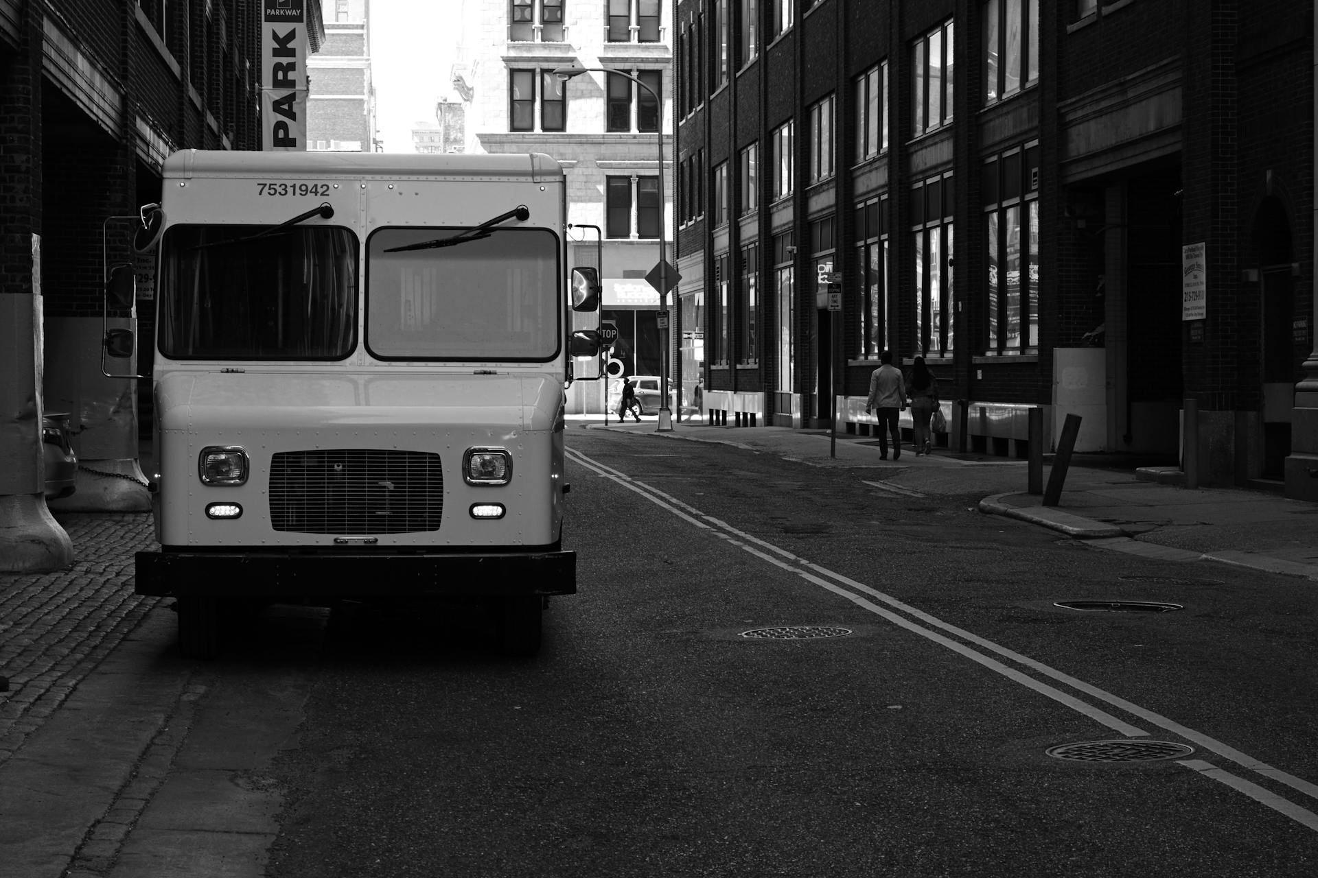 A monochrome view of a city street featuring a parked delivery truck and pedestrians walking.