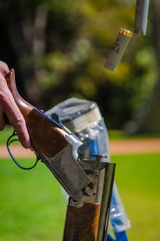 Detailed view of a shotgun ejecting spent shells during target practice in a grassy outdoor area.