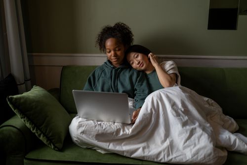 Free Two women enjoying a cozy moment on a couch with a laptop, embracing love and technology. Stock Photo