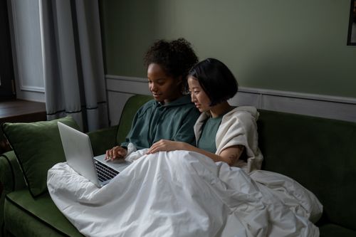Free Two women enjoying togetherness under a blanket, watching a laptop indoors. Stock Photo