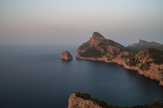 A breathtaking aerial view of a rocky coastline during sunrise, captured with tranquil waters and scenic cliffs.