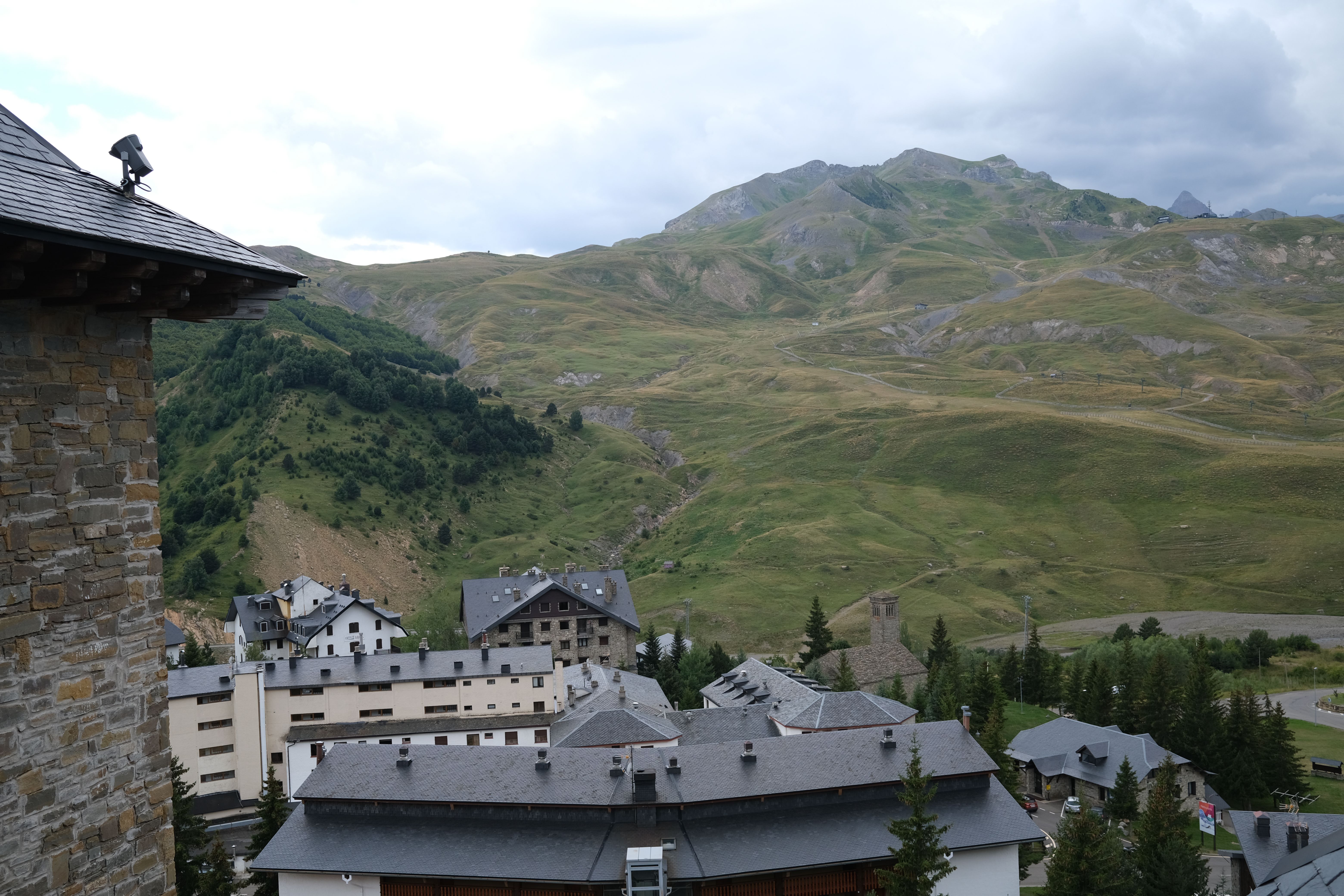 Picturesque view of a mountain village with rustic buildings and lush hills under overcast skies.