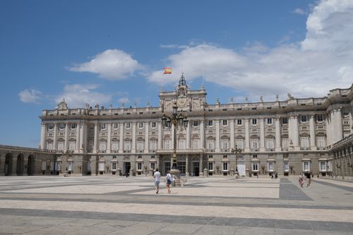 Free A wide view of the Royal Palace of Madrid with people and the Spanish flag under a blue sky. Stock Photo