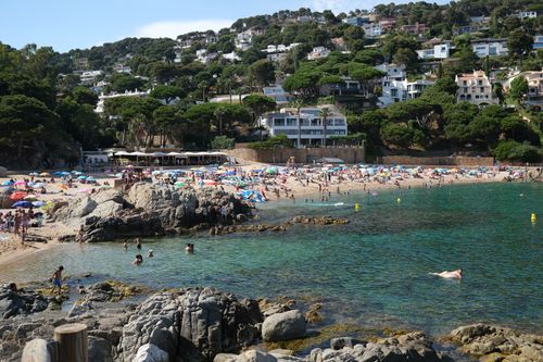 Free Crowded summer beach scene with turquoise waters and houses on Costa Brava. Stock Photo