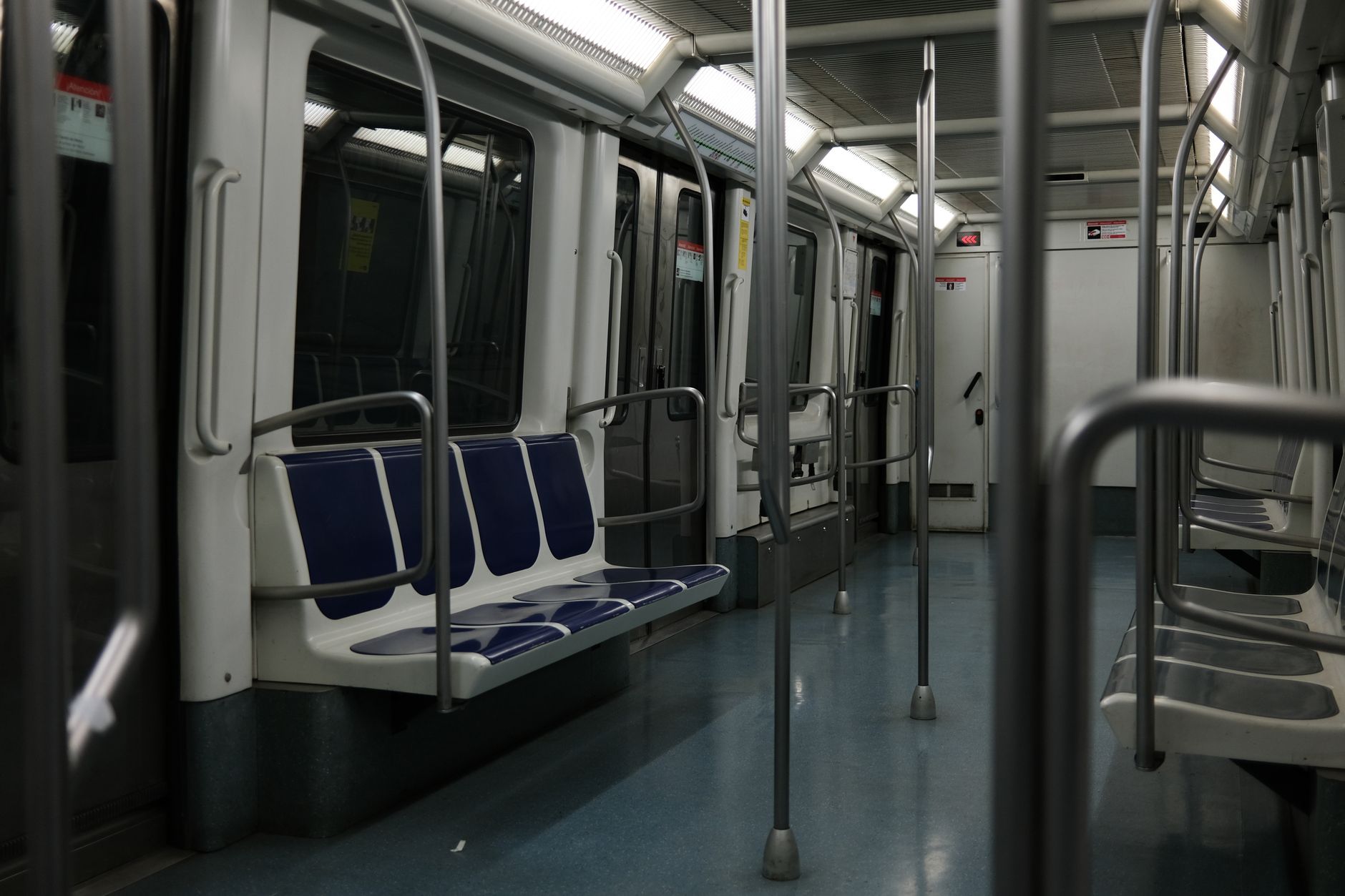 A quiet subway car interior with blue seats and metal poles, captured in soft lighting.