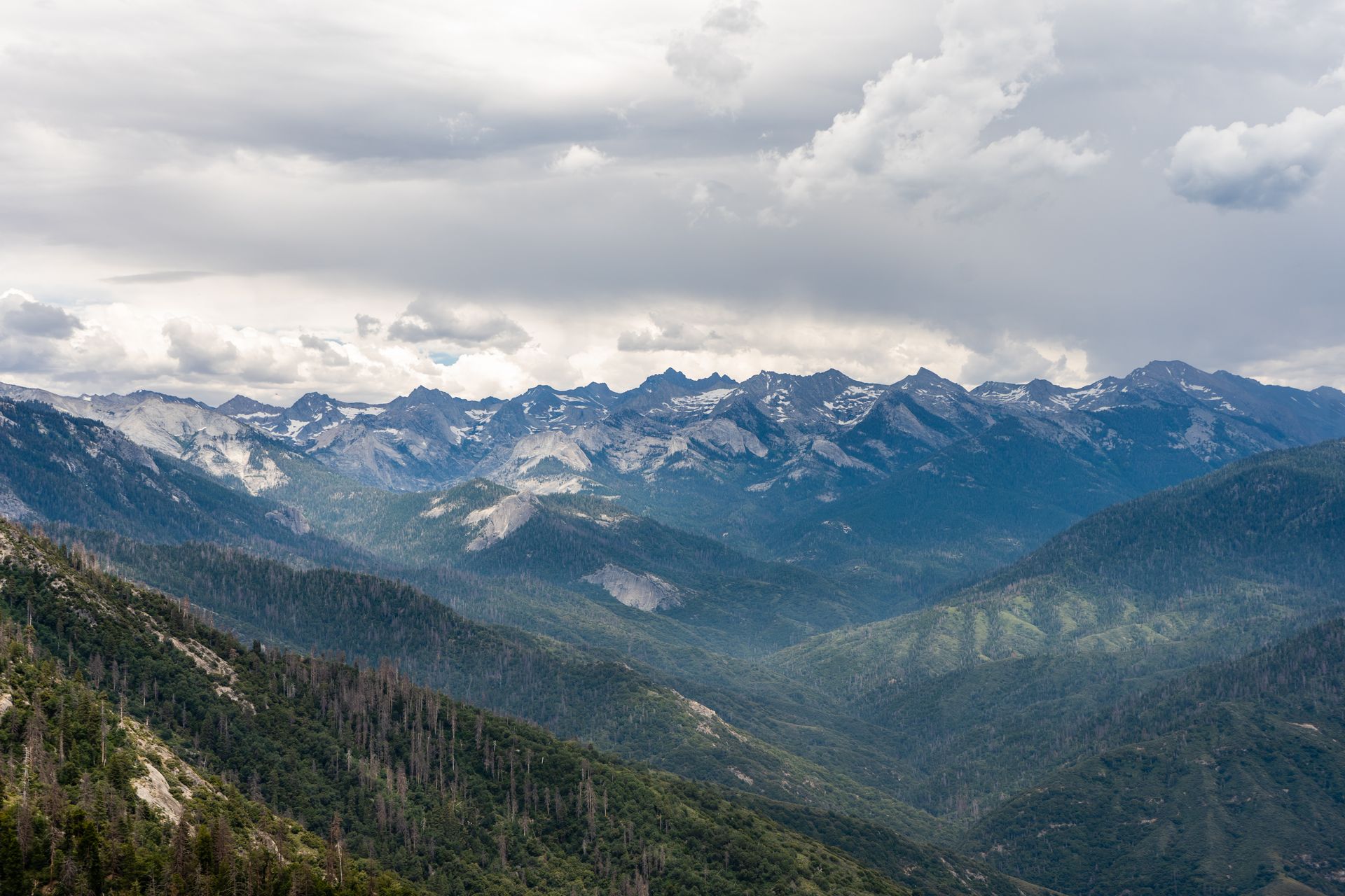 Expansive view of a mountain range with lush valleys under a cloudy sky, ideal for nature lovers.