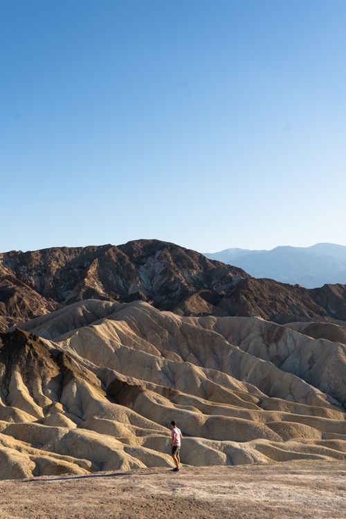 Free A lone hiker explores the rugged terrain of Zabriskie Point under a clear blue sky in Death Valley. Stock Photo