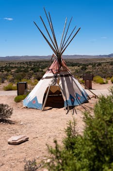 A traditional teepee stands in an arid desert landscape under a bright clear sky, embodying indigenous culture.