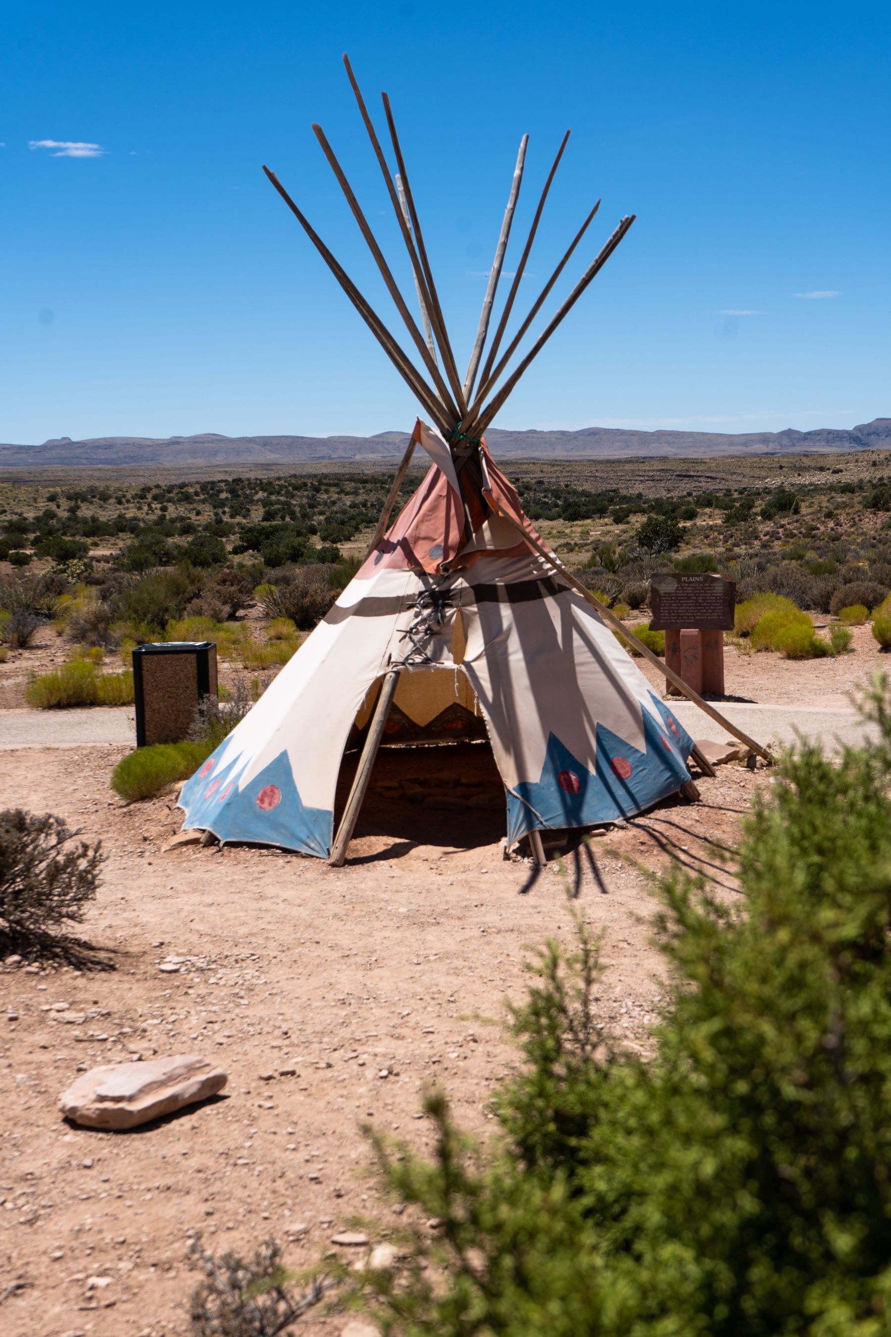 Traditional teepee in an arid desert landscape beneath a clear blue sky.