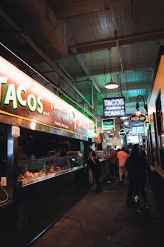 Indoor market scene with taco stalls and neon lights, lively atmosphere for dining and shopping.