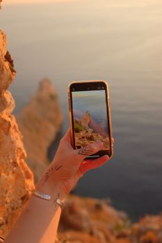 A close-up of a smartphone capturing a scenic coastal view during sunset.