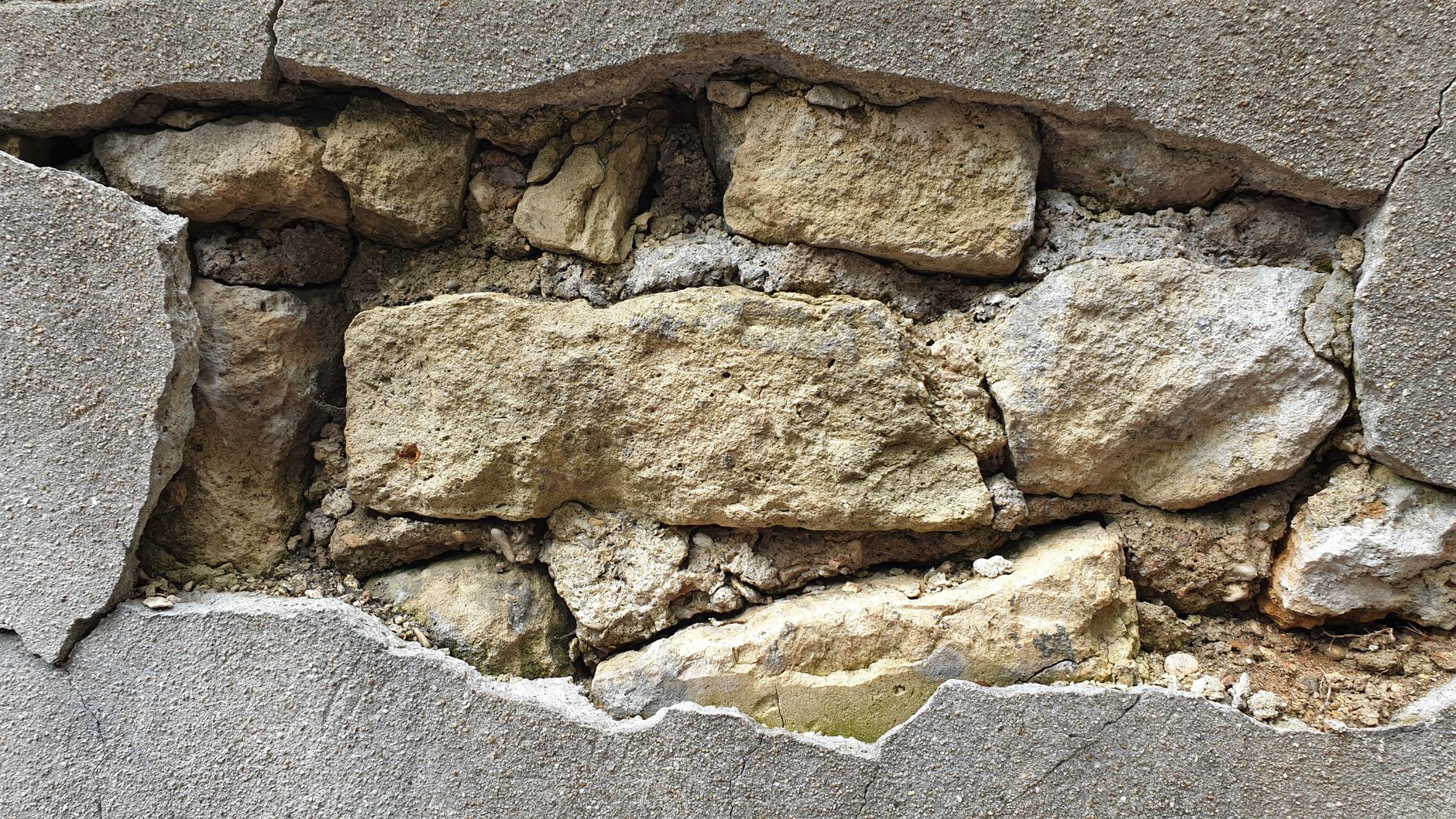 Detailed view of a cracked concrete wall exposing the underlying stonework and texture.