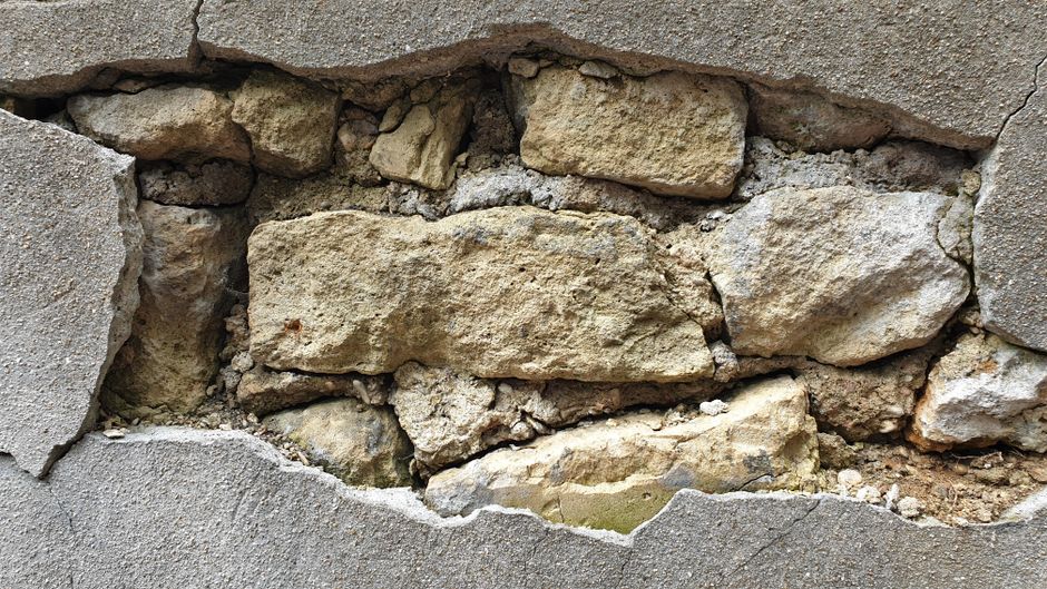 Detailed view of a cracked concrete wall exposing the underlying stonework and texture.