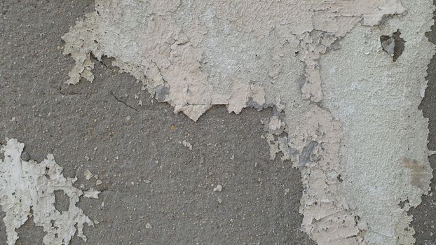 Close-up of a worn concrete wall with peeling paint texture revealing underlying surface.