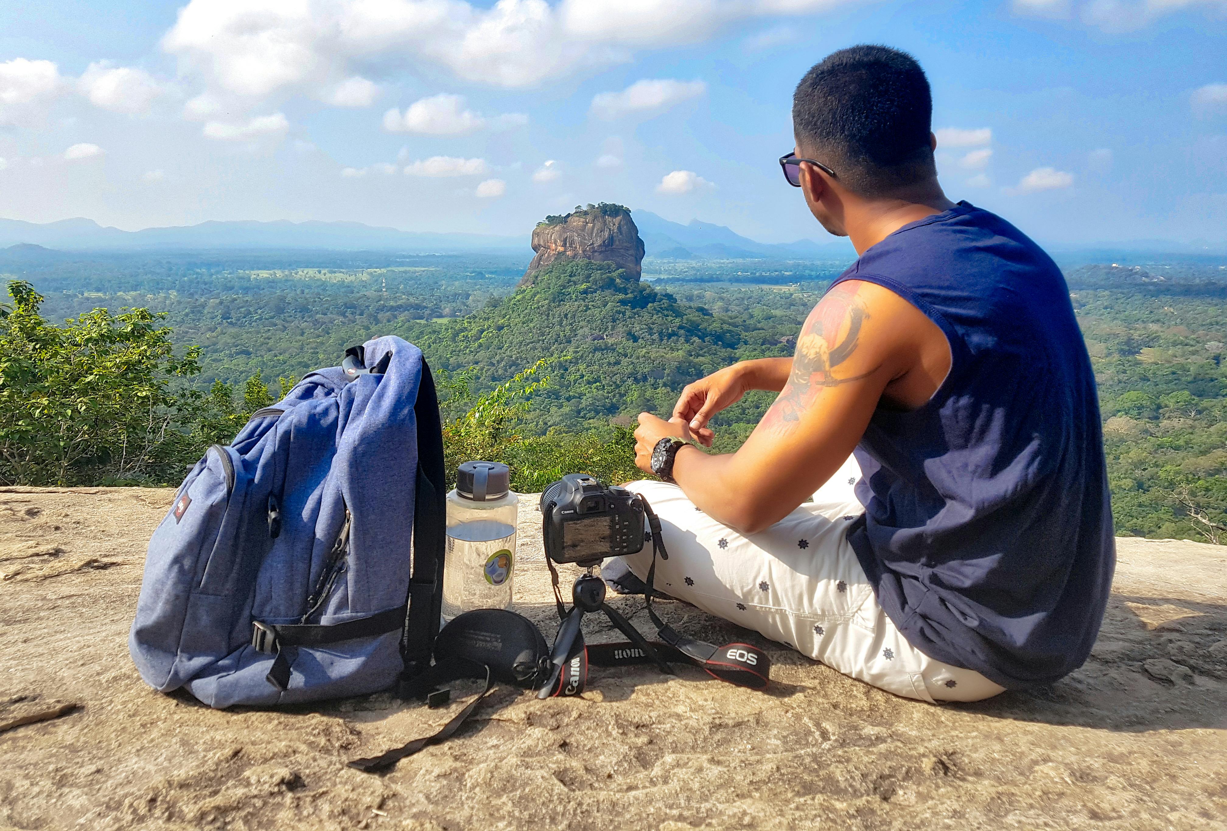 Man Sitting on Top of Gray Cliff Mountain Beside Backpack, Water Bottle, and Camera · Free Stock ...