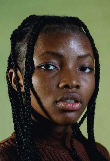 Close-up portrait of an adult woman with braided hair against a green background.