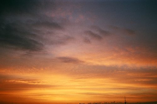 Free Vibrant orange and dark clouds highlight a sunset sky, creating a warm and dramatic view. Stock Photo