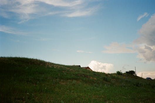 Idyllic rural landscape featuring a grassy hill under a serene blue sky with clouds.
