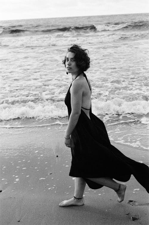 Free Woman in Black Backless Dress Walking on Beach Stock Photo