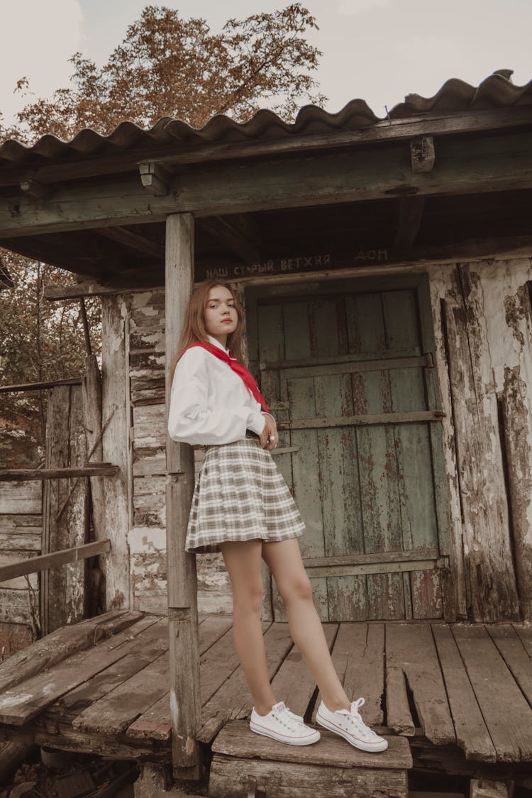 A Woman Wearing A Plaid Skirt Leaning On A Post