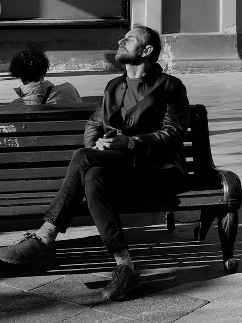 Grayscale Photo of a Man Sitting on a Bench Enjoying the Sun
