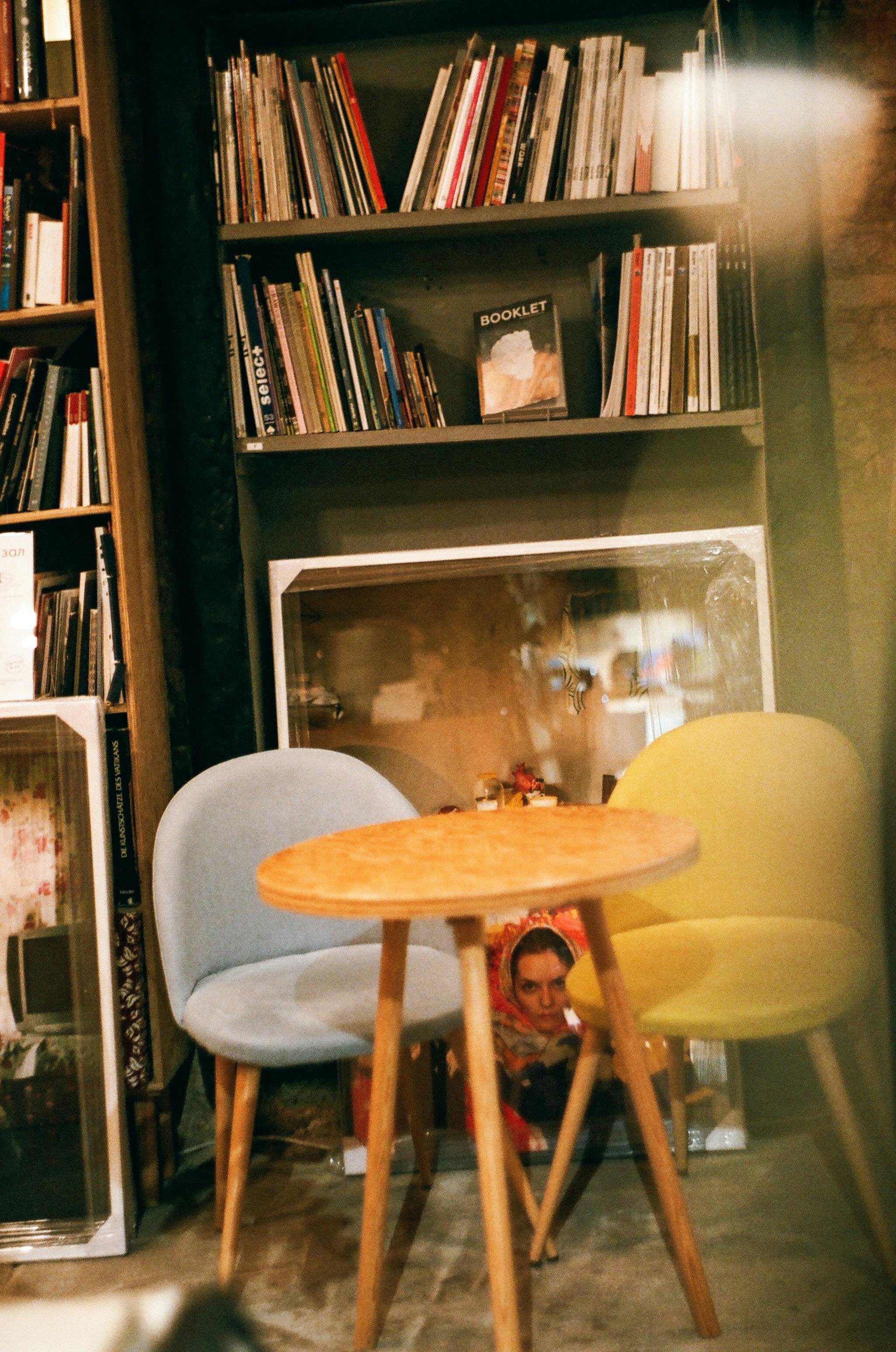 A cozy indoor reading nook featuring modern chairs, a wooden table, and a bookshelf full of books.