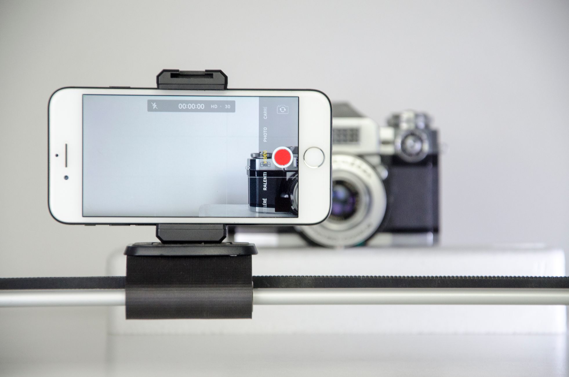 Close-up of smartphone recording in front of a vintage camera, perfect for videography and tech enthusiasts.
