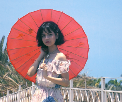 阳光明媚的日子里，一位穿着花卉连衣裙的时尚女人撑着红伞