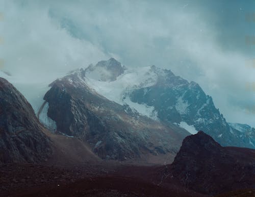 Snow Covered Rocky  Mountain Under Cloudy Sky