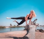 晴朗的日子里，一名身穿黑色运动服的健硕女子在万里无云的蓝天下，手扶倒在小溪岸边的树干做体操