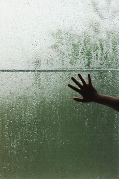 A hand touching a raindrop-covered window, creating a contemplative mood.