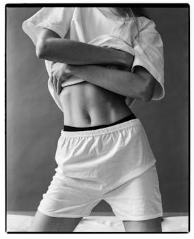 Black and white photograph of a woman in sportswear with arms crossed, focusing on the midsection.