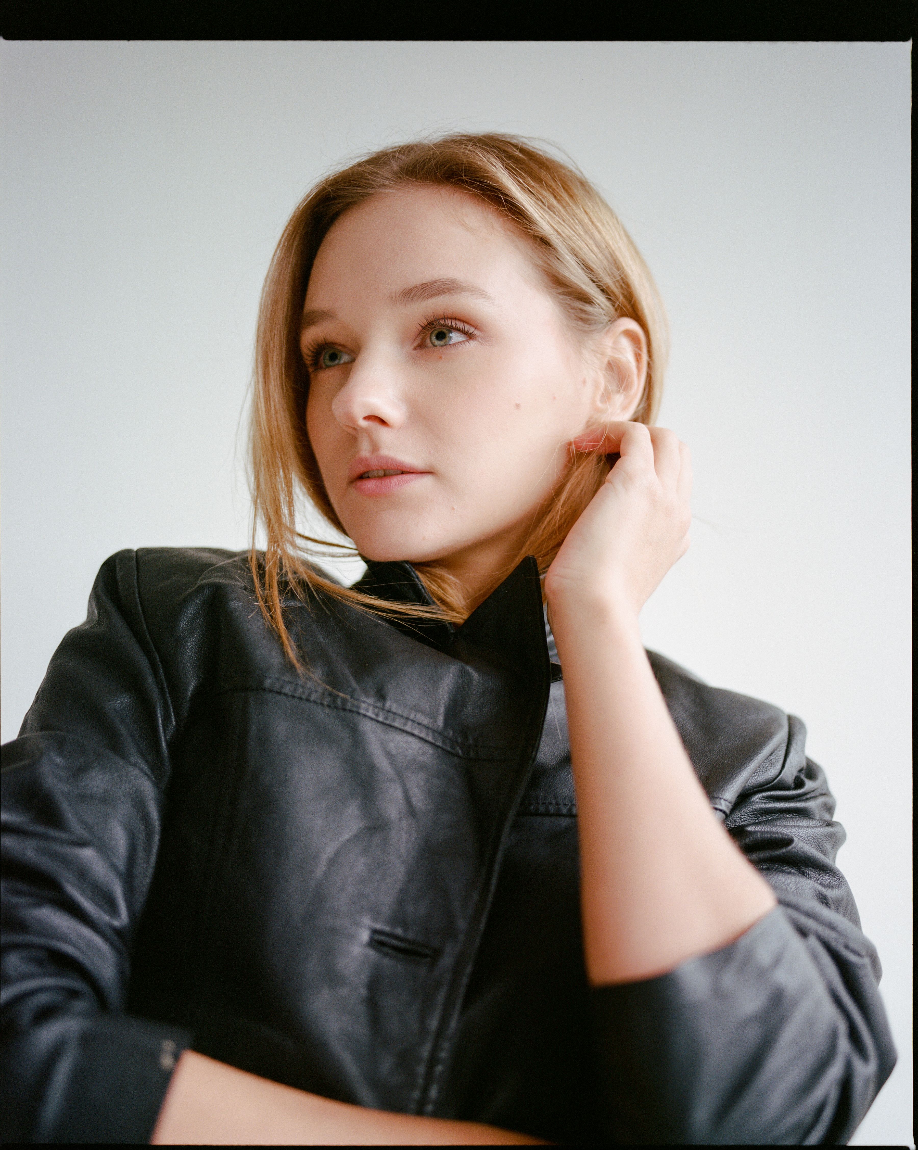 Elegant portrait of a woman in a black leather jacket with a soft white background.